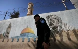 Un policier palestinien passe devant une peinture murale du défunt dirigeant historique palestinien Yasser Arafat, dans la ville de Hébron en Cisjordanie occupée, le 11 novembre 2024, à l'occasion du 20e anniversaire de la mort d'Arafat