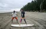 Mohammad Mannan (G) donne un cours de surf à un débutant, sur la plage de Cox's Bazar, dans le sud-est du Bangladesh, le 22 juin 2026