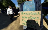 Un homme porte une pancarte sur laquelle il est écrit "Vénézuéliens à la recherche d'un emploi", dans un campement de fortune près d'une gare de bus, le 9 août 2018 à Quito, en Equateur