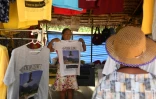 Une vendeuse montre à des touristes un "t-shirt souvenir" du sauvetage des adolescents en 2018 dans la grotte inondée de Tham Luang, le 13 juin 2019 à Mae Sai, en Thaïlande