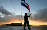 Un militant tient un drapeau cubain sur le pont du bateau de pêche Maguro, faisant partie de la flottille d'aide humanitaire, à son arrivée dans le port de La Havane, le 24 mars 2026