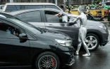 L'artiste de rue Ari Munandar (d), le corps recouvert de peinture argentée, fait la manche sous la pluie à un carrefour de Jakarta, le 1er avril 2025 en Indonésie