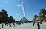Des passants regardent la Patrouille de France (PAF) survoler la pyramide du Louvre conçue par l'architecte sino-américain Ieoh Ming Pei, le 9 juillet 2025 à Paris, lors d'une répétition du défilé annuel du 14 juillet