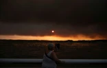 Une femme observe la fumée depuis la plage à Andernos-les-Bains lors d'un incendie dans la forêt de Lège-Cap-Ferret, dans le sud-ouest de la France, le 23 juillet 2026, alors qu'une partie de la zone voisine a été évacuée