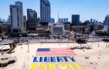 Un drapeau américain dessiné sur une plage de Tel-Aviv devant un bâtiment de l'ambassade des Etats-Unis, accompagné des mots "Liberté pour tous" pour réclamer la libération des otages retenus à Gaza, le 4 juillet 2025, jour anniversaire de l'indépendance des Etats-Unis
