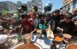 Des Palestiniens font la queue pour obtenir un repas chaud lors d'une distribution assurée par une cuisine soldiaire au camp de réfugiés de Nousseriat, dans le centre de la bande de Gaza, le 5 mai 2025