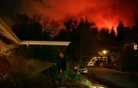 Un homme arrose devant sa maison alors que les flammes de l'incendie du secteur de Pacific Palisades progressent vers le quartier d'Encino à Los Angeles, aux Etats-Unis, le 10 janvier 2024