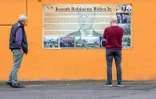 Des piétons lisent un panneau d'information sous un portrait géant du candidat à la présidentielle américaine Joe Biden sur la maison de ses ancêtres, le 7 octobre 2020 à Ballina, en Irlande