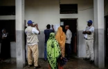 Des observateurs électoraux (g et d) regardent des habitants consulter les listes électorales à l'entrée d'un bureau de vote à Moroni, le 14 janvier 2024 aux Comores