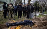 Un prêtre et des proches devant le corps exhumé du maire de Gostomel, Yuriy Prylypko, qui a été enterré près d'une église dans le village de Gostomel, dans la région de Kiev, le 12 avril 2022