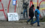 Des réfugiés passent devant un graffiti de l'artiste de rue Banksy représentant en migrant le fondateur d'Apple, Steve Jobs, à l'époque de l'évacuation complète du camp de la "Jungle" de Calais, à Calais, le 24 octobre 2016