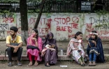 Des étudiants assis devant un mur couvert de graffitis dénonçant les violences politiques et policières, le 11 août 2024 à Dacca au Bangladesh