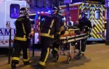 Photo prise à l'aube du 14 novembre 2015 montrant des pompiers en train d'évacuer un homme près du Bataclan, l'une des cibles des attaques terroristes qui ont coûté la vie à 130 personnes et fait fait plus de 400 blessés à Paris