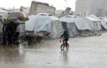 Un enfant palestinien sur une bicyclette sous la pluie devant des tentes trempées dans un camp de fortune de la ville de Gaza, le 31 décembre 2024