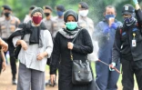 Un agent de sécurité pulvérise du désinfectant sur les familles de victimes du coronavirus au cimetière de Pondok Ranggon, le 6 mai 2020 à Jakarta, en Indonésie