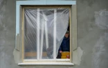 Un homme regarde au travers d'une fenêtre faite de plastique dans une maison endommagée par les tirs des forces russes à Bachtanka près de Mykolaïv, dans le sud de l'ukraine, le 27 mars 2022
