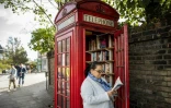 Patsy Ari feuillette un livre près d'une ancienne cabine téléphonique reconvertie en bibliothèque d'échange, à Londres, le 21 octobre 2017