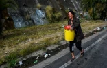 Une femme porte un seau rempli d'eau pour l'utiliser dans ses toilettes, le 1er avril 2019 à Petare, un quartier de Caracas, au Venezuela