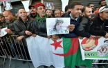 Des Algériens se rassemblent avec le drapeau national et des portraits de l'ancien chef militaire algérien, le général Ahmed Gaïd Salah, devant le Palais du Peuple en prévision de ses funérailles à Alger le 25 décembre 2019