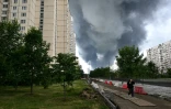 Une femme marche dans un quartier résidentiel tandis que de la fumée noire s'élève du site de la raffinerie russe de Gazprom Neft, située dans la banlieue sud-est de Moscou, le 18 juin 2026. L'Ukraine a mené tot le 18 juin une attaque de drones "de grande envergure" contre Moscou, plusieurs d'entre eux ayant atteint une raffinerie de pétrole, a déclaré le maire de la ville, Sergueï Sobianine.