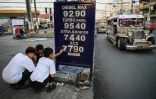 Des employés changent le prix des carburants dans une station-service de Manille, le 17 mars 2026 aux Philippines