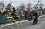 Un homme à moto passe à côté d'un bâtiment détruit dans le village de Moschchun, au nord-ouest de Kiev, le 20 avril 2022
