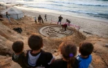 Des enfants regardent une sculpture de sable proclamant "Bienvenue au ramadan", le 17 février 2026 sur une plage au sud de la bande de Gaza