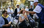 Des volontaires distribuent l'hostie aux fidèles en fauteuils roulants, lors de la messe célébrée par le pape Léon XIV sur la prairie du sanctuaire de Lourdes, le 27 septembre 2026