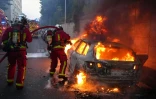 Des pompiers tentent d'éteindre une voiture en feu en marge d'une manifestation à Nanterre,  théâtre d'incidents en soirée, le 27 juin 2023