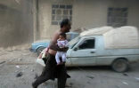 Un homme avec un bébé s'enfuit après des bombardements sur Kafr Batna, dans la banlieue de Damas, le 30 septembre 2016