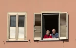 Un couple à sa fenêtre écoute la messe des Rameaux célebrée en face de chez lui sur le toit d'une église à Rome, le 5 avril 2020 