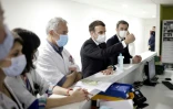 Emmanuel Macron (C), le ministre de la Santé Olivier Véran (D), et le Dr Jan Hayon (G) parlent avec le personnel soignant de l'unité de soins intensifs de l'hôpital de Poissy, le 17 mars 2021