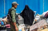 Un membre des forces de sécurité kurdes surveille une femme qui s'apprête à quitter le camp d'al-Hol qui accueille des proches de combattants présumés du groupe État islamique (EI), le 3 septembre 2023 dans le nord-est de la Syrie