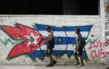 Deux jeunes passent devant un mur arborant un drapeau cubain, le 14 juillet 2026 à La Havane, lors d'une panne d'électricité nationale à Cuba
