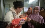Une femme porte un enfant qui a surcévu à un glissement de terrain dans le village de Pasirlangu, dans la région du Bandung occidental, au sud-est de Jakarta, le 24 janvier 2026