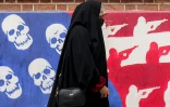 Une femme passe devant un mur de l'ancienne ambassade des Etats-Unis à Téhéran, peint aux couleurs du drapeau américain avec les étoiles remplacées par des têtes de mort et les rayures par des silhouettes de soldats, le 8 avril 2025