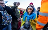 Des réfugiés, dont une femme portant
un drapeau ukrainien, s'apprêtent à monter dans un bus à destination de la frontière entre l'Ukraine et la Pologne le 18 mars 2022 à Medyka (Pologne)