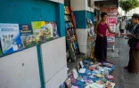 Le bouquiniste Tin Than (à gauche) montre un livre à un client devant son étal installé à même la rue de Pansodan, dans la capitale birmane Rangoun, le 5 décembre 2018