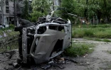 Un petit garçon fait de la balançoire près d'une voiture calcinée à Mariupol le 29 mai 2022
