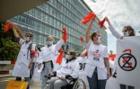 Des professionnels de santé du mouvement Extinction Rebellion agitent des rubans rouges lors d'une manifestation devant les locaux de l'OMS à Genève, le 29 mai 2021