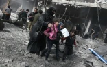 Une femme et des enfants cherchent un abri après des bombardements sur la ville de Hamouria, dans l'enclave rebelle de la Ghouta orientale, près de Damas le 19 février 2018