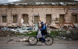 Un homme à vélo passe devant une maison détruite dans le village ukrainien de Derhachi, au nord de Kharkiv, dans l'est de l'Ukraine, le 27 avril 2022