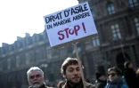 Un homme brandit une pancarte "Droit d'asile en marche arrière - Stop" dans une manifestation organisée par l'OFPRA contre la loi asile et immigration, le 21 février 2018 à Paris
