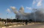 De la fumée lors d'une frappe israélienne alors que des Palestiniens marchent sur une route utilisée pour atteindre un point de distribution d'aide de la Fondation humanitaire de Gaza (GHF,) près du camp de réfugiés de Nousseirat, dans le centre de la bande de Gaza, le 25 juin 2025