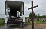 Des employés municipaux retirent les sacs mortuaires de l'arrière d'un conteneur de morgue pour les déposer dans des cercueils, dans un cimetière de la ville de Boutcha, dans la région de Kyiv, le 11 août 2022