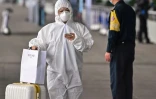 Un voyageur en tenue intégrale de protection contre le coronavirus prépare son smartphone pour passer les contrôles à son arrivée à l'aéroport Tianhe, le 11 avril 2020 à Wuhan, dans la province chinoise du Hubei
