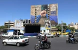Des véhicules devant un panneau d'affichage sur la façade d'un bâtiment représentant le détroit d'Ormuz avec une légende en persan disant "À jamais dans la main de l'Iran", place Vanak à Téhéran, le 25 mai 2026