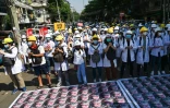 Du personnel médical et des étudiants manifestent contre le coup d'Etat à Rangoun, le 5 mars 2021, devant des photos du chef de la junte, le général Min Aung Hlaing, collées à même le bitume, dans le but de freiner la progression des soldats, réticents à marcher sur le visage de leur chef