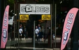 Des passants se tiennent devant la vitrine d'un magasin annonçant des réductions à l'occasion des soldes d'été, à Béziers, dans l'Hérault, le 28 juin 2025