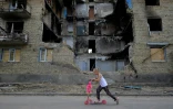 Une enfant en trottinette passe devant un immeuble détruit par des bombardements, le 4 juin 2022 à Gorenka, près de Kiev, en Ukraine